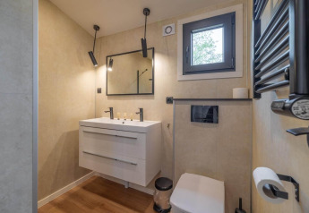Baño moderno en un lodge con lavabo doble, espejo cuadrado, ventana, inodoro y luces colgantes elegantes.