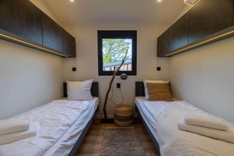 Moderne lodgekamer met twee enkele bedden, bovenkasten, houten vloer en raam met zicht op bomen.