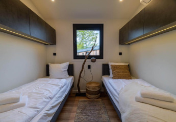 Moderne lodgekamer met twee enkele bedden, bovenkasten, houten vloer en raam met zicht op bomen.