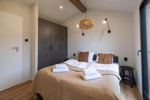 Chambre de lodge confortable avec lit double, couverture beige, lampe suspendue et armoire encastrée.