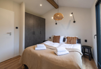 Accogliente stanza di lodge con letto matrimoniale, coperta beige, lampada in vimini e armadio a muro.