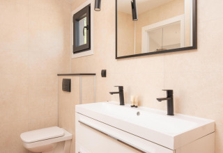 Baño moderno en una cabaña con inodoro de pared, lavabo doble, grifería negra y espejo grande.