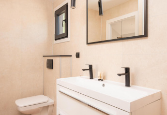 Baño moderno en una cabaña con inodoro de pared, lavabo doble, grifería negra y espejo grande.