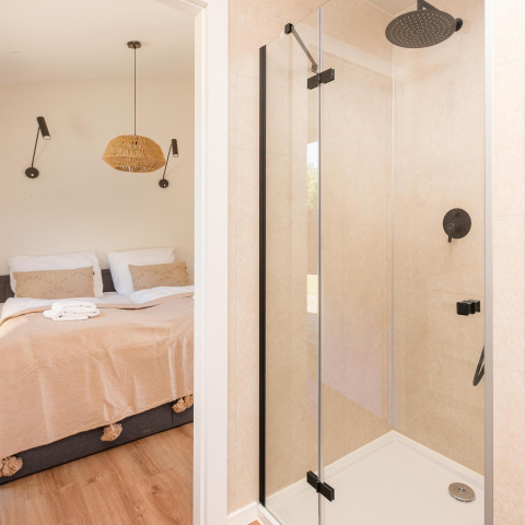 Modern lodge-interieur met glazen douche en zicht op een gezellig slaapkamer door de deuropening.