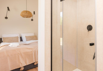 Modern lodge-interieur met glazen douche en zicht op een gezellig slaapkamer door de deuropening.
