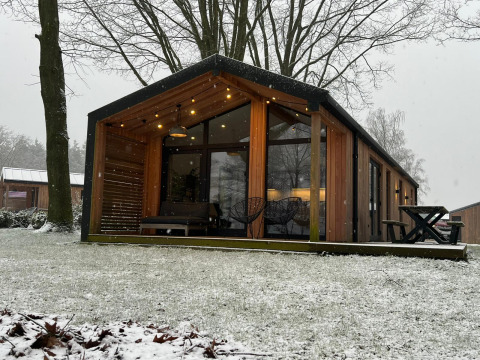 Cabaña moderna de madera en Wilsumer Berge, Alemania, rodeada de nieve y árboles de invierno desnudos.