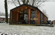 Modern wooden lodge at Wilsumer Berge, Germany, with a snowy yard and bare winter trees in the background.