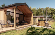 Cabaña de madera moderna con terraza cubierta, asientos al aire libre y bañera exterior en plena naturaleza.