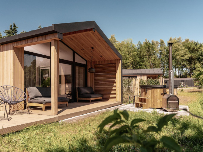 Cabaña de madera moderna con terraza cubierta, asientos al aire libre y bañera exterior en plena naturaleza.