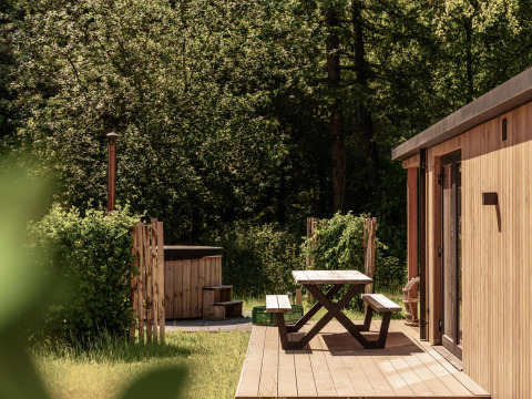 Buiten terras met picknickbank bij Nature Lodge en hot tub, omringd door groene bomen en bos.