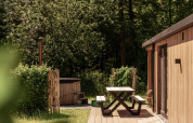 Buiten terras met picknickbank bij Nature Lodge en hot tub, omringd door groene bomen en bos.