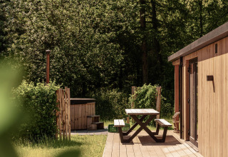 Buiten terras met picknickbank bij Nature Lodge en hot tub, omringd door groene bomen en bos.