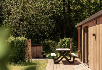 Buiten terras met picknickbank bij Nature Lodge en hot tub, omringd door groene bomen en bos.