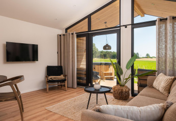 Sala de estar de lodge moderno con grandes ventanales, vistas al campo, muebles de madera y plantas.