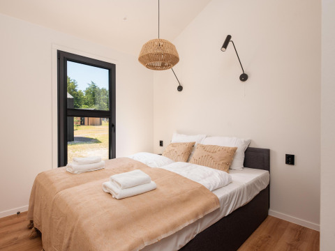 Habitación luminosa en una cabaña con cama doble, ropa de cama beige, ventana grande y lámparas modernas.