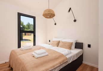 Habitación luminosa en una cabaña con cama doble, ropa de cama beige, ventana grande y lámparas modernas.