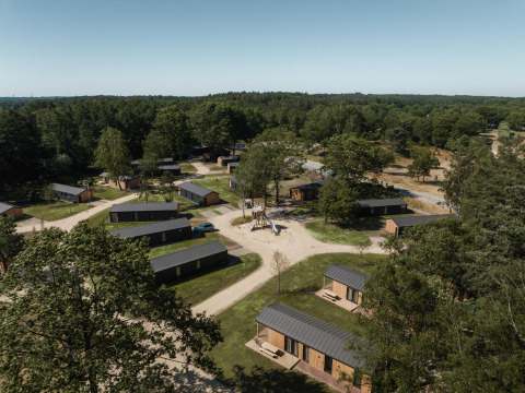 Luchtfoto van een lodge met kleine houten chalets, omringd door bos en wandelpaden onder een heldere hemel.