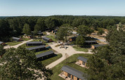 Luftaufnahme einer Lodge mit mehreren Holzhütten im Wald, umgeben von Bäumen und schmalen Wegen.