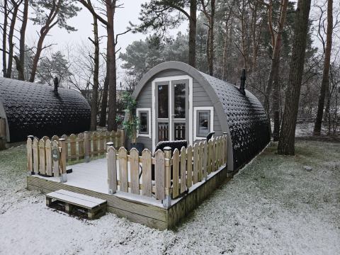 Verschneite Holzhütte mit Veranda im Wald, aufgenommen bei Woodlodge in Wilsumer Berge, Deutschland.