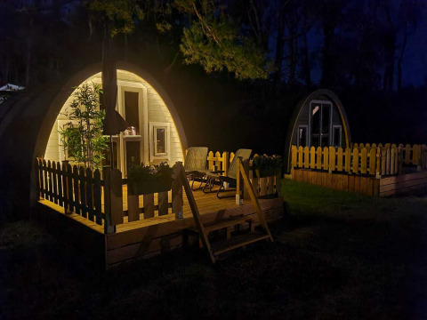Nattebillede af oplyst hytte med terrasse og stole, Woodlodge på Wilsumer Berge, Tyskland.