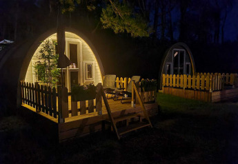 Nattebillede af oplyst hytte med terrasse og stole, Woodlodge på Wilsumer Berge, Tyskland.