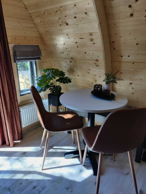 Innenraum einer Holzhütte mit runden Wänden, zwei braunen Stühlen, Tisch und Pflanzen am Fenster.