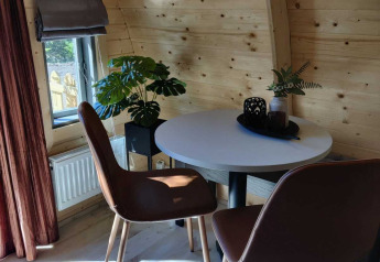 Intérieur d’un chalet en bois avec murs arrondis, deux chaises brunes, table ronde et plantes vertes.