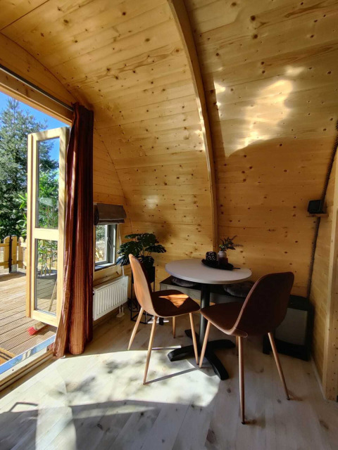 Interior de cabaña de madera en Woodlodge, Wilsumer Berge, Alemania, con mesa, sillas y ventana abierta.