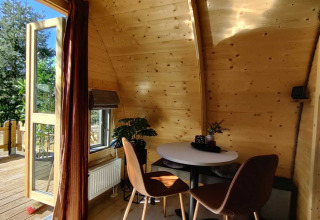 Interior de cabaña de madera en Woodlodge, Wilsumer Berge, Alemania, con mesa, sillas y ventana abierta.