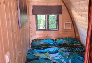 Dormitorio con paneles de madera en Woodlodge, Wilsumer Berge, Alemania, con cama doble y ventana al jardín.