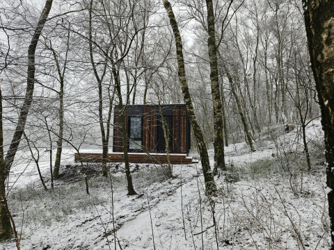 Nokken NKN-18 Cabin i Wilsumer Berge, Tyskland, omgivet af sneklædte træer i en vinterlig skov.