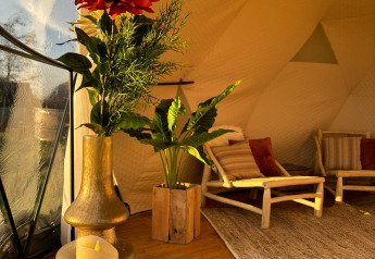 Arredo accogliente nel Cast Away Dome con fiori, candele e sedie in legno a TinyParks Cast Away, Paesi Bassi.