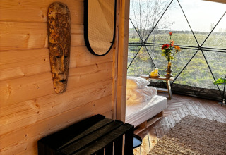 Interieur van Cast Away Dome natuurhuisje met hout, bed en uitzicht op het groen in Nederland.