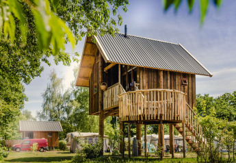 Baumhaus mit runder Terrasse in einem grünen, sonnigen Umfeld, ideal für einen naturnahen Urlaub.