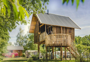 Boomhut met ronde houten veranda in een groene, bosrijke omgeving, ideaal voor een rustgevend verblijf.