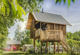 Casa del árbol de madera con balcón circular, rodeada de naturaleza y árboles, ideal para relajarse.