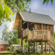 Casa sull’albero in legno con balcone rotondo, immersa nel verde, perfetta per una vacanza nella natura.