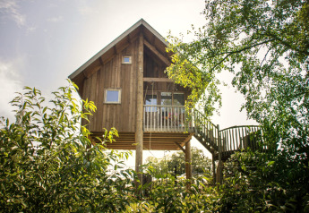 Baumhaus im Holiday Park Mölke in den Niederlanden, umgeben von grünen Bäumen und sonnigem Himmel.