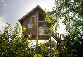 Træhus i Holiday Park Mölke, Holland, omgivet af grønne træer og buske, med trappe og altan.