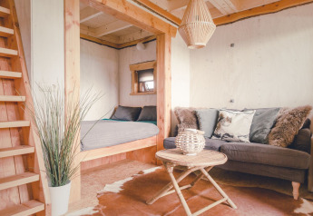 Knusse boomhut met grijze bank, ronde tafel en slaapnis in Holiday Park Mölke in Nederland.