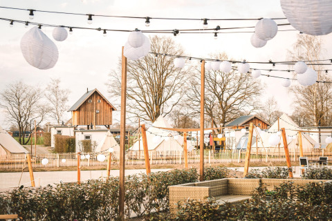 Tree house and tents at Holiday Park Mölke in the Netherlands, decorated with hanging lights and lanterns.