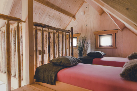 Gemütlicher Schlafbereich im Baumhaus mit zwei Einzelbetten, Holzwänden und kleinen Fenstern bei Holiday Park Mölke.