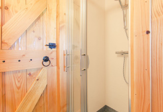 Pequeña cabina de ducha con puerta de cristal y pared de madera rústica en Tree house, Holiday Park Mölke, Países Bajos.