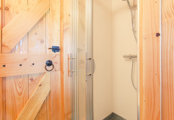 Kleine douchecabine met glazen deur en rustiek houten interieur in de Tree house bij Holiday Park Mölke, Nederland.