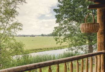 Uitzicht vanuit een boomhut bij Holiday Park Mölke in Nederland met weilanden, rivier en mand.