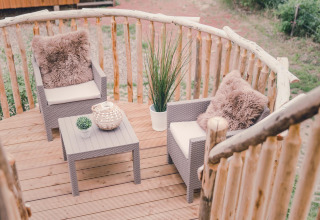 Baumhaus-Balkon mit zwei Sesseln, Tisch, Dekokissen und Pflanzen im Holiday Park Mölke, Niederlande.