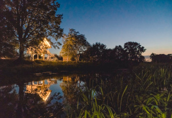 Beleuchtetes Baumhaus am See im Ferienpark Mölke, Niederlande, umgeben von Bäumen in der Abenddämmerung.