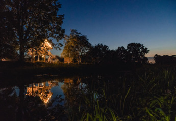 Verlicht boomhuis bij vijver in Vakantiepark Mölke, Nederland, omringd door bomen bij schemering.