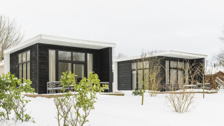 Twee zwarte moderne chaletjes met grote ramen in de sneeuw bij Holiday Park Mölke, Nederland.