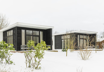 To moderne hytter med sorte facader og store vinduer står omgivet af sne ved Holiday Park Mölke, Holland.